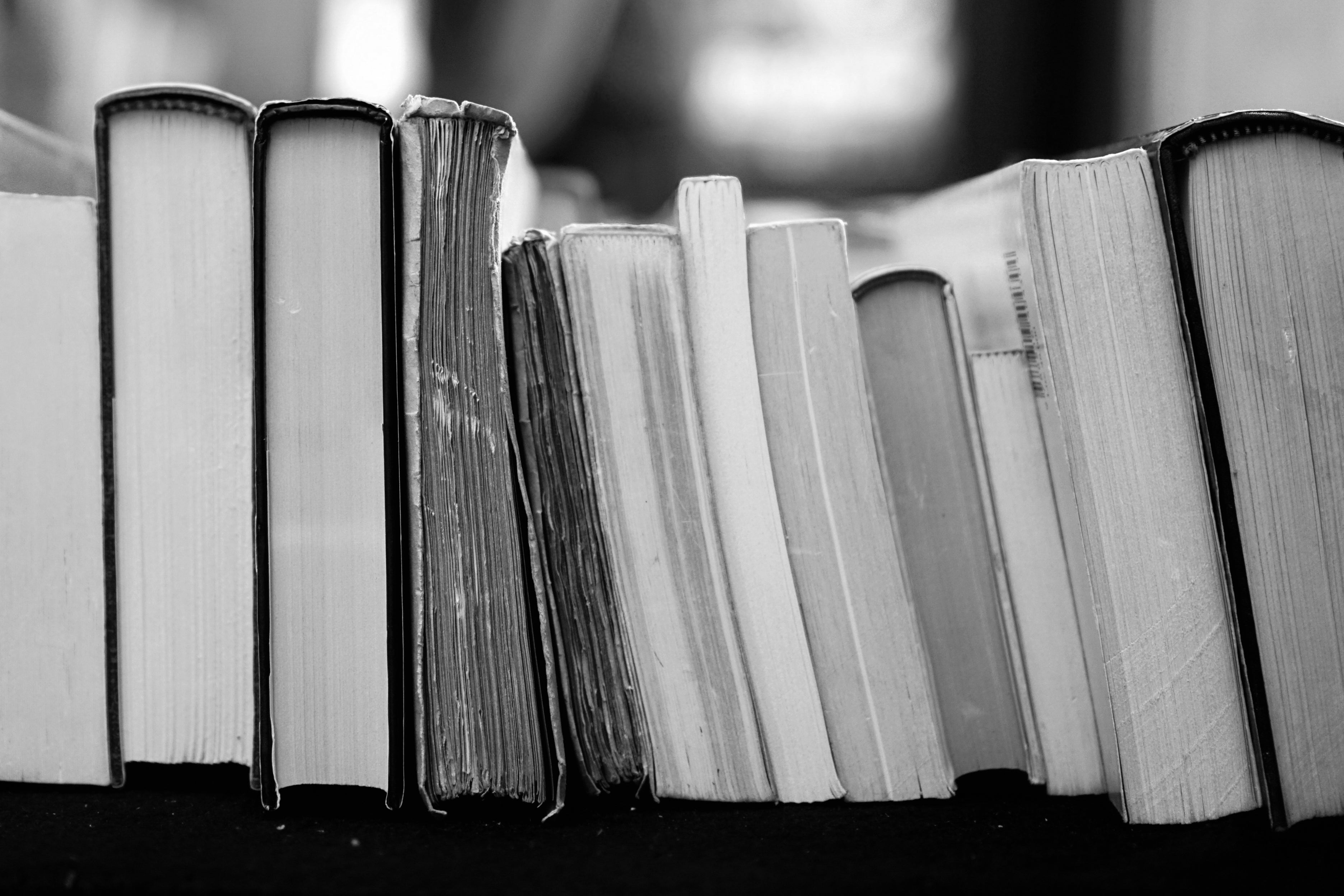 Black and white photo of a row of standing books, showing varying sizes and worn covers.