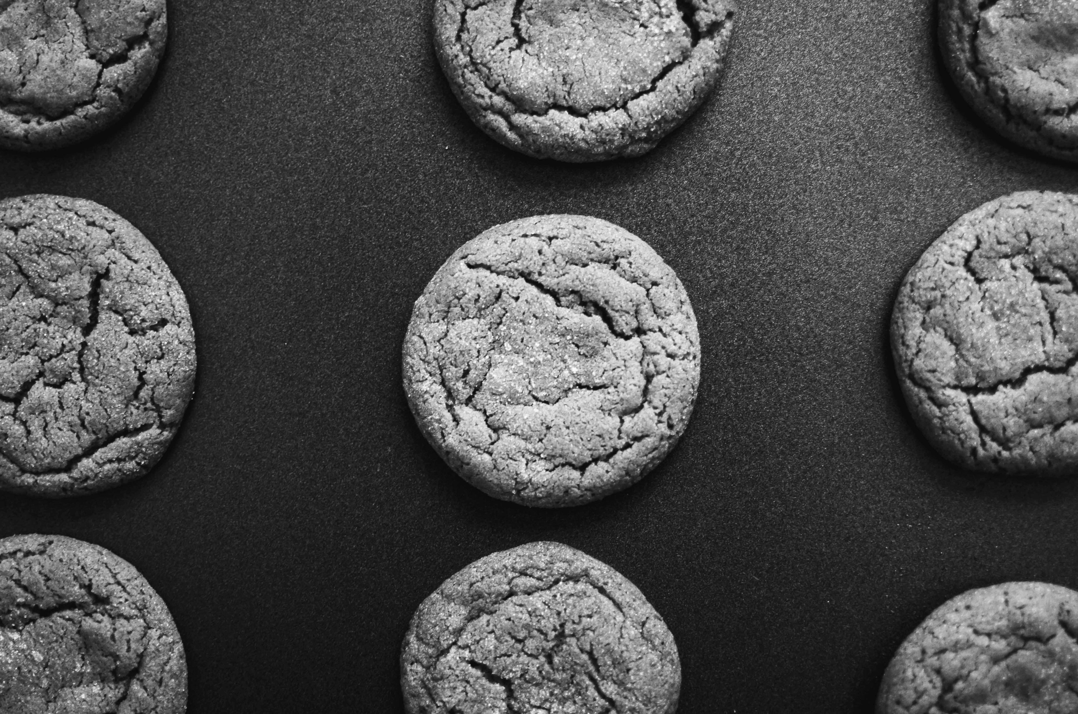 Black and white photo of freshly baked cookies arranged in a grid pattern on a dark surface.