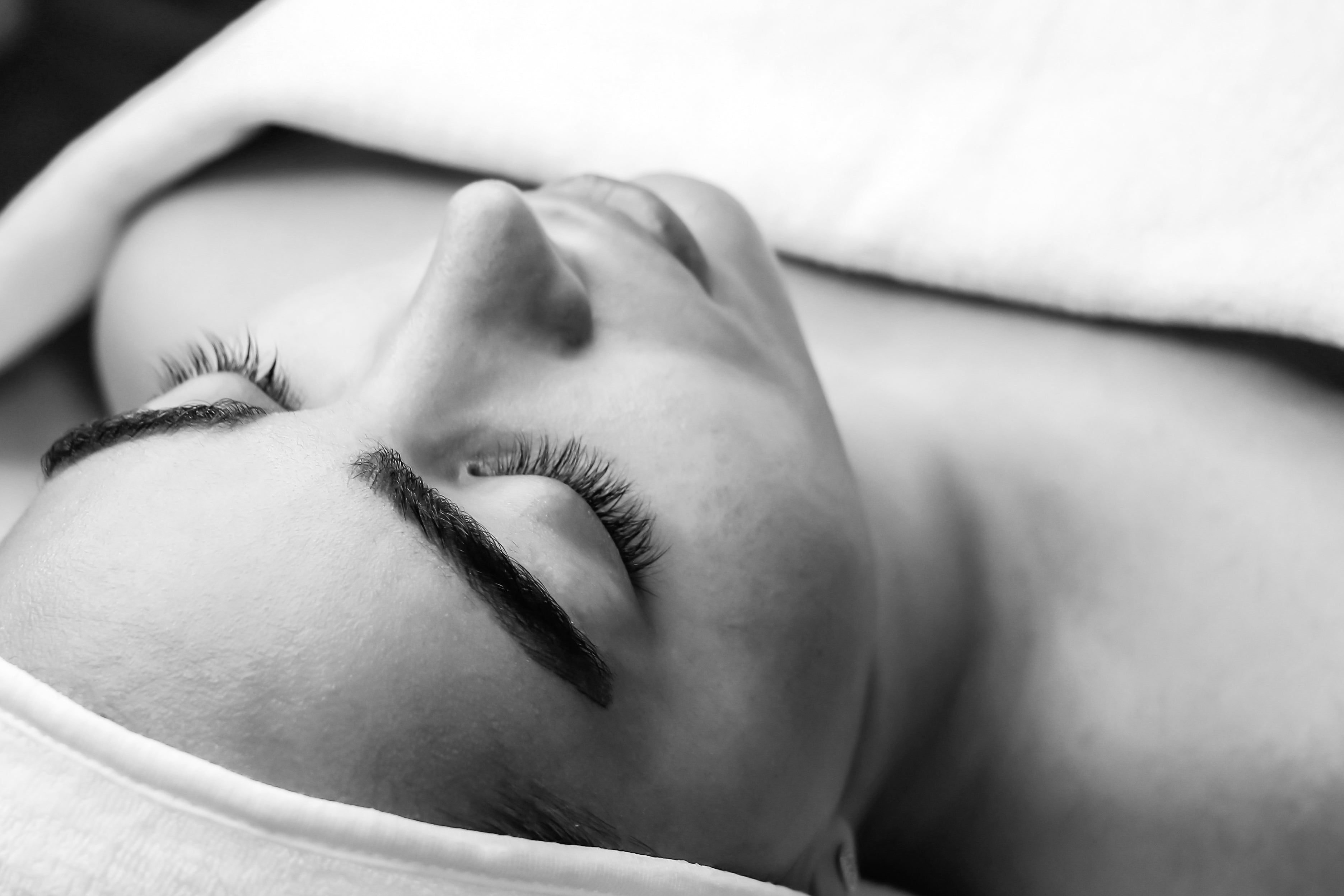 Relaxed woman reclining with a towel, eyes closed, in a serene spa setting.