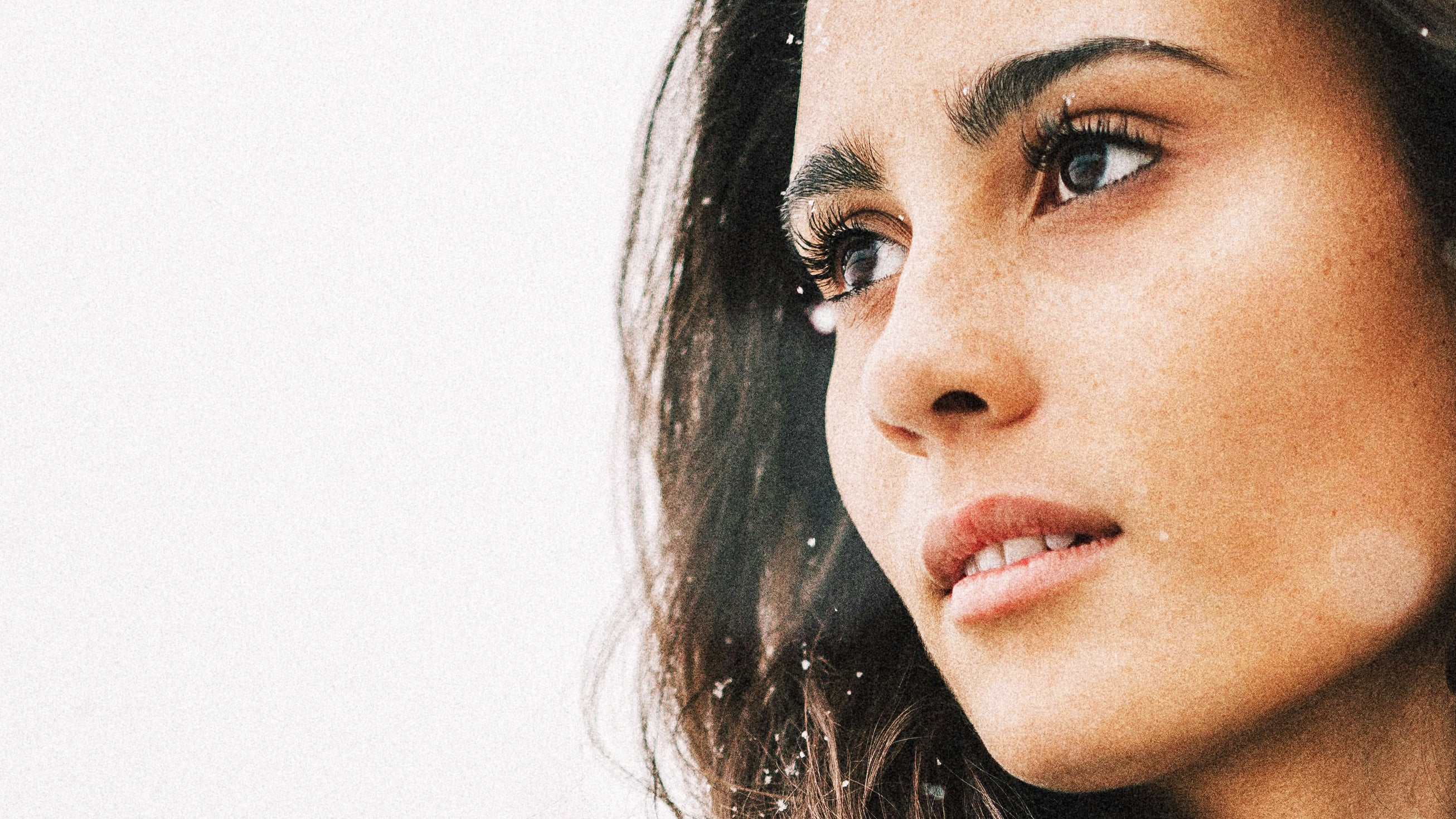 Profile of a woman with clear skin, gazing into the distance, snowflakes visible in her hair.