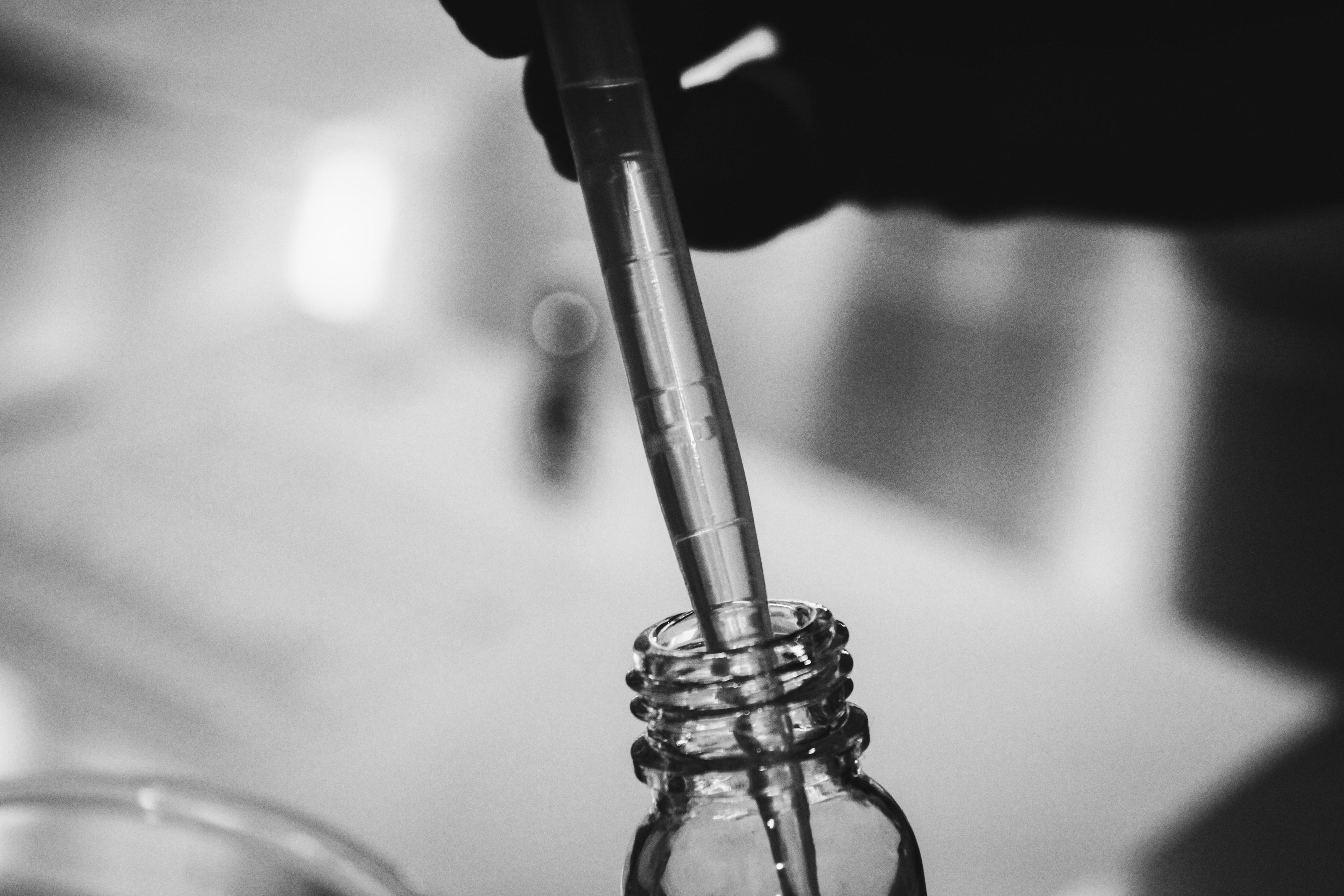 Black and white photo of a dropper being used to extract liquid from a glass bottle, representing a skincare serum.