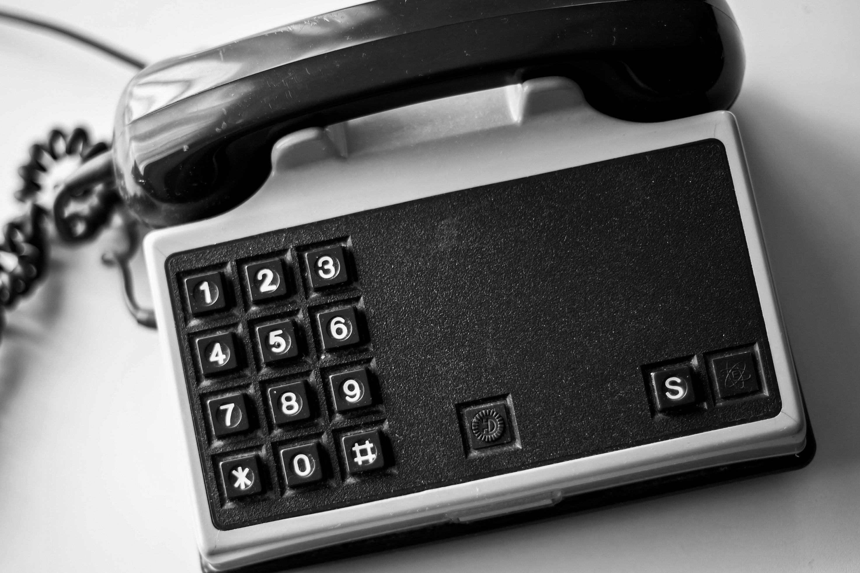 Black and white photo of a vintage telephone with a rotary dial keypad and coiled cord.