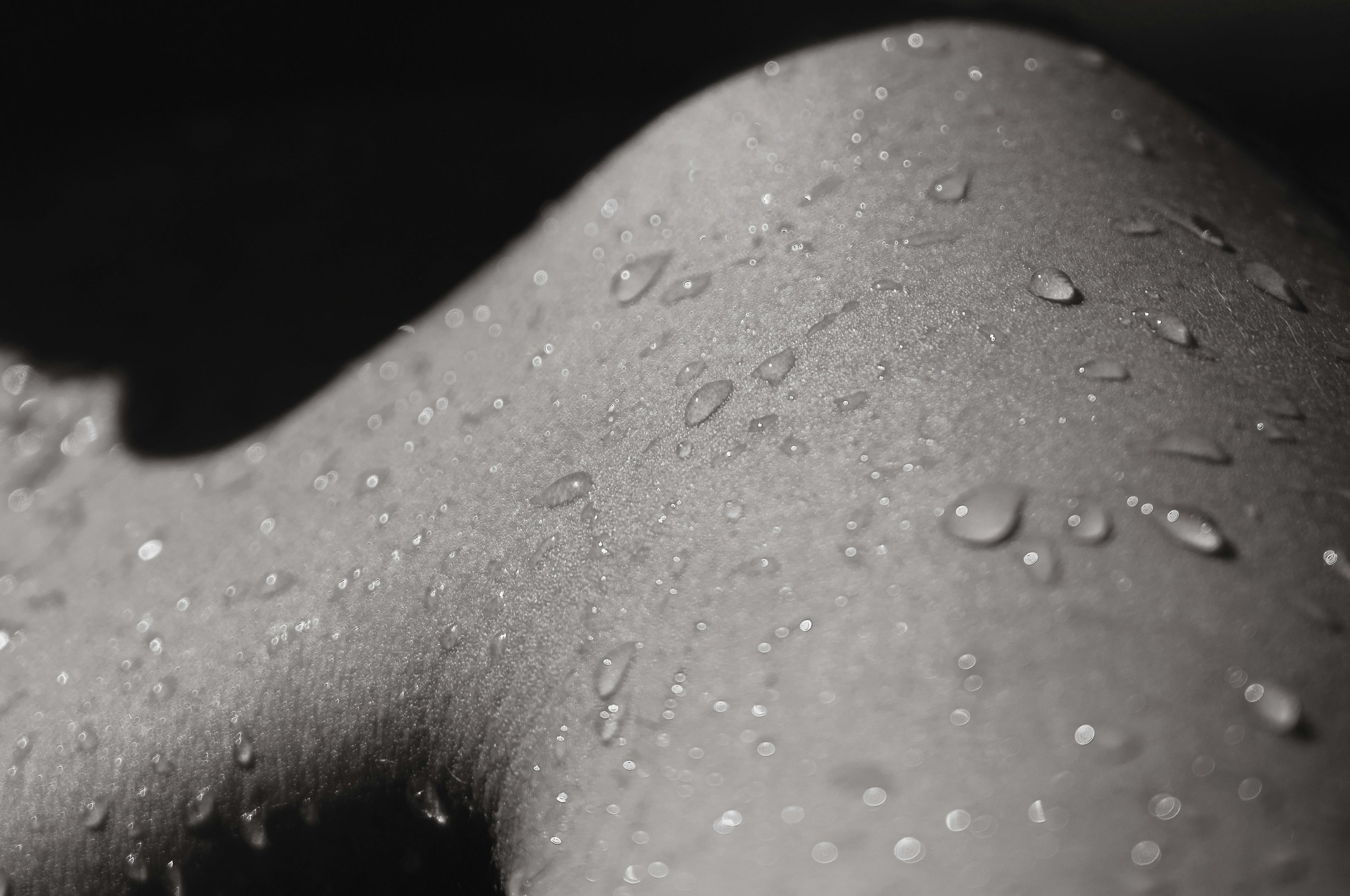 Close-up of water droplets on smooth skin, highlighting texture and hydration in a black and white photo.